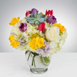 Round glass vase with white hydrangeas, roses, colorful tulips, yellow blooms, lilac and a central succulent