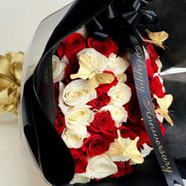 Bouquet of red and white roses wrapped in black paper with gold butterfly accents