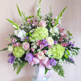 Large pastel floral arrangement in a white vase with a pink ribbon