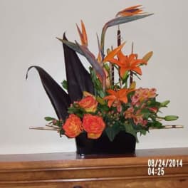 Orange lilies and roses in a black vase with tall dark leaves