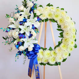 White floral funeral wreath on an easel with blue ribbon