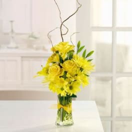 Yellow flower bouquet in a clear glass vase with curly branches