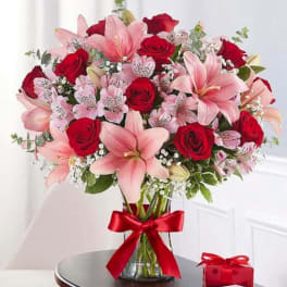 Bouquet of pink lilies and red roses in a glass vase with a red ribbon