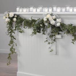 White floral garland with trailing greenery and ribbon draped over a mantel
