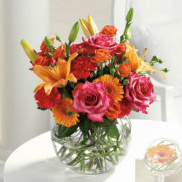 Mixed bouquet of pink roses, orange lilies, and gerbera daisies in a glass vase