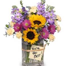 Bouquet of sunflowers, purple flowers, and cream blooms in a glass vase