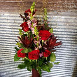 Tall arrangement of red roses and pink snapdragons in a burgundy vase