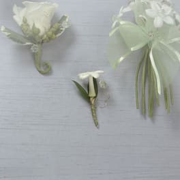 White floral boutonnieres and a small corsage on a pale background