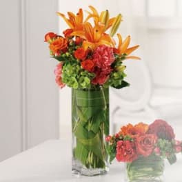 Tall vase arrangement with orange lilies, red roses, and green hydrangeas