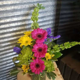 Bright mixed bouquet with pink gerberas, yellow daisies, and purple filler in a glass vase