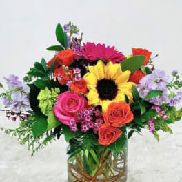 Colorful mixed bouquet in a clear glass vase with a sunflower and roses