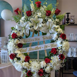 Large funeral wreath with red roses, white lilies, and white mums on an easel