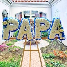 Floral letters spelling PAPA on an easel with white and blue flowers