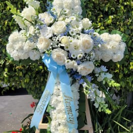 White floral standing cross on an easel with a blue ribbon