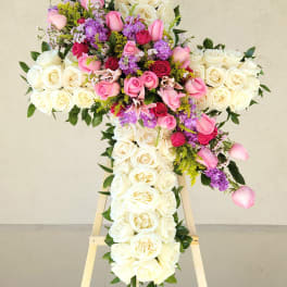 Large cross-shaped floral arrangement of white, pink, and purple roses on an easel