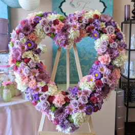 Large heart-shaped floral wreath on a wooden easel in pink, purple, and white.