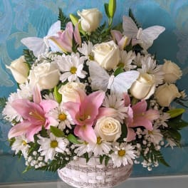 Basket arrangement of white roses, pink lilies, and daisies with butterfly accents