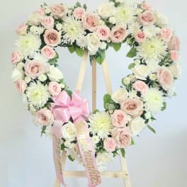 Heart-shaped floral wreath of pink and white roses on a wooden easel