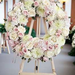 Heart-shaped floral wreath of white and pink roses on a wooden easel