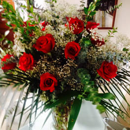 Tall arrangement of red roses with white filler flowers in a clear glass vase