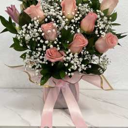 Pink roses and white baby's breath arranged in a pink box with ribbon.
