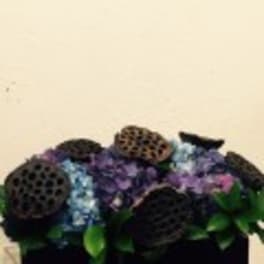 Dark floral arrangement with purple and blue blooms in a black container