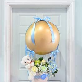 Baby gift basket with flowers, teddy bear, and gold balloon