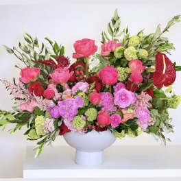 Bright pink and red floral arrangement in a white pedestal vase