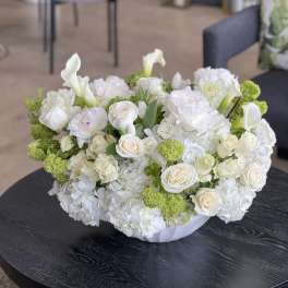 White floral arrangement with roses, calla lilies, and green pom-pom blooms in a low vase