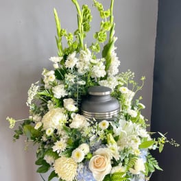 White floral funeral arrangement with a gray urn centerpiece