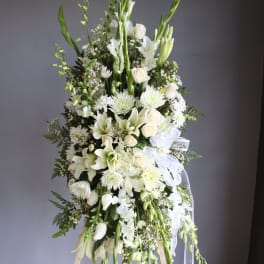 Tall white floral standing spray with lilies, roses, and ribbons