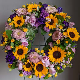 Circular wreath of sunflowers, roses, and purple blooms on a stand