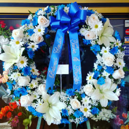 Large floral wreath with white lilies, roses, and blue ribbon.