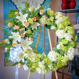 Large floral wreath with white lilies, roses, and green hydrangeas on an easel