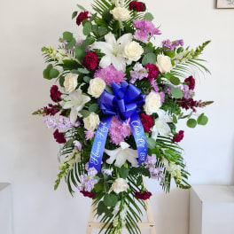 Tall funeral spray with white lilies, roses, and purple flowers on an easel