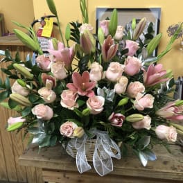 Pink roses and lilies arranged in a basket with a white ribbon