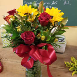 Bouquet of red roses and yellow sunflowers in a glass vase with a red ribbon