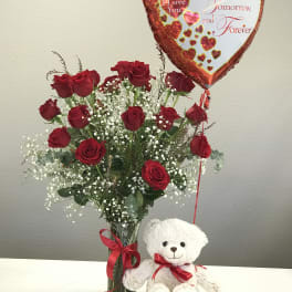 Red roses in a glass vase with a heart balloon and teddy bear