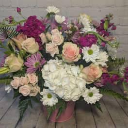 Mixed bouquet of roses, hydrangea, and daisies in a pink container
