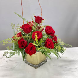 Red roses arranged in a clear square vase with greenery