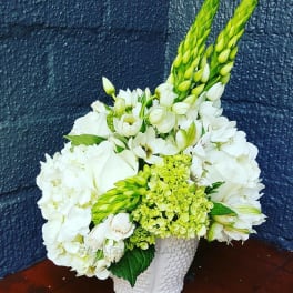 White floral arrangement in a textured white vase with green accents