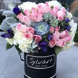 Pink roses, white hydrangeas, and purple blooms in a black hatbox