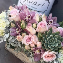 Pink roses and purple orchids arranged with succulents in a wooden box