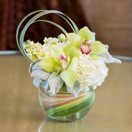 Yellow orchids and white hydrangeas in a glass vase with curved loops