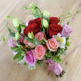 Hand-tied bouquet of red and pink roses with white blooms and ribbon