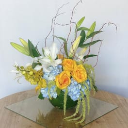 Arrangement of yellow roses, white lilies, and blue hydrangeas in a green vase