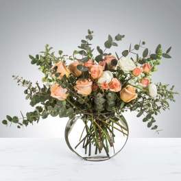 Peach and white roses in a round glass vase with airy greenery