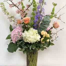 Tall mixed bouquet in a clear glass vase with pink, white, and purple blooms