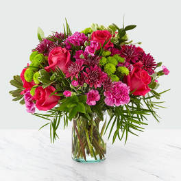 Pink roses and mixed magenta flowers in a clear glass vase
