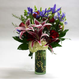 Bouquet of lilies, roses, and irises in a green glass vase